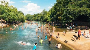 A river with people swimming and walking along the banks.