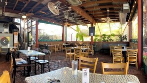 An outdoor restaurant with wooden tables and chairs, a brick floor, and large windows.
