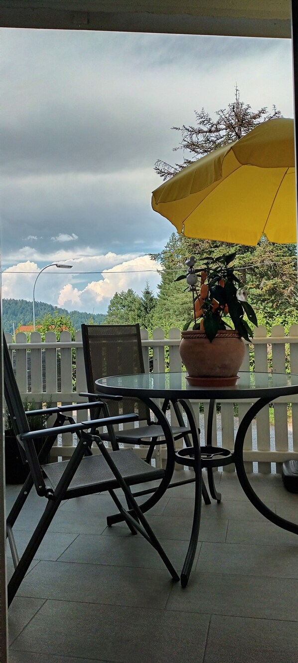 A patio with a glass table, black chairs, a yellow umbrella, and a potted plant.