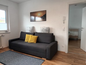 Un salon moderne avec un canapé gris, deux coussins, un tapis bleu et un tableau accroché au mur.