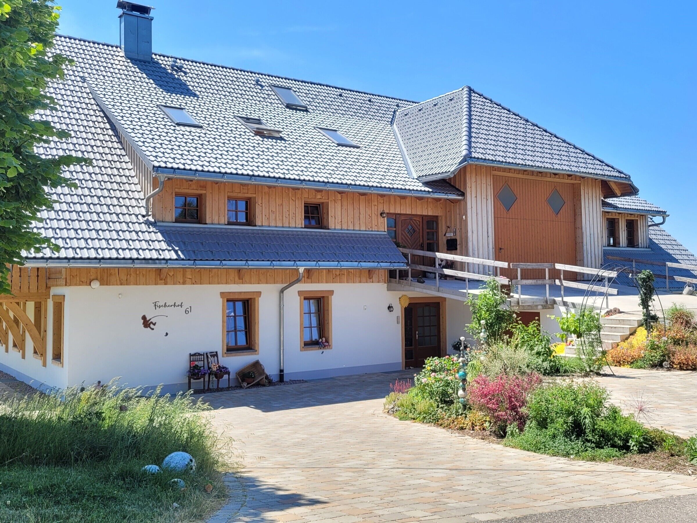 A two-story building with a sloped roof, wooden exterior, and a small garden area with plants and flowers.