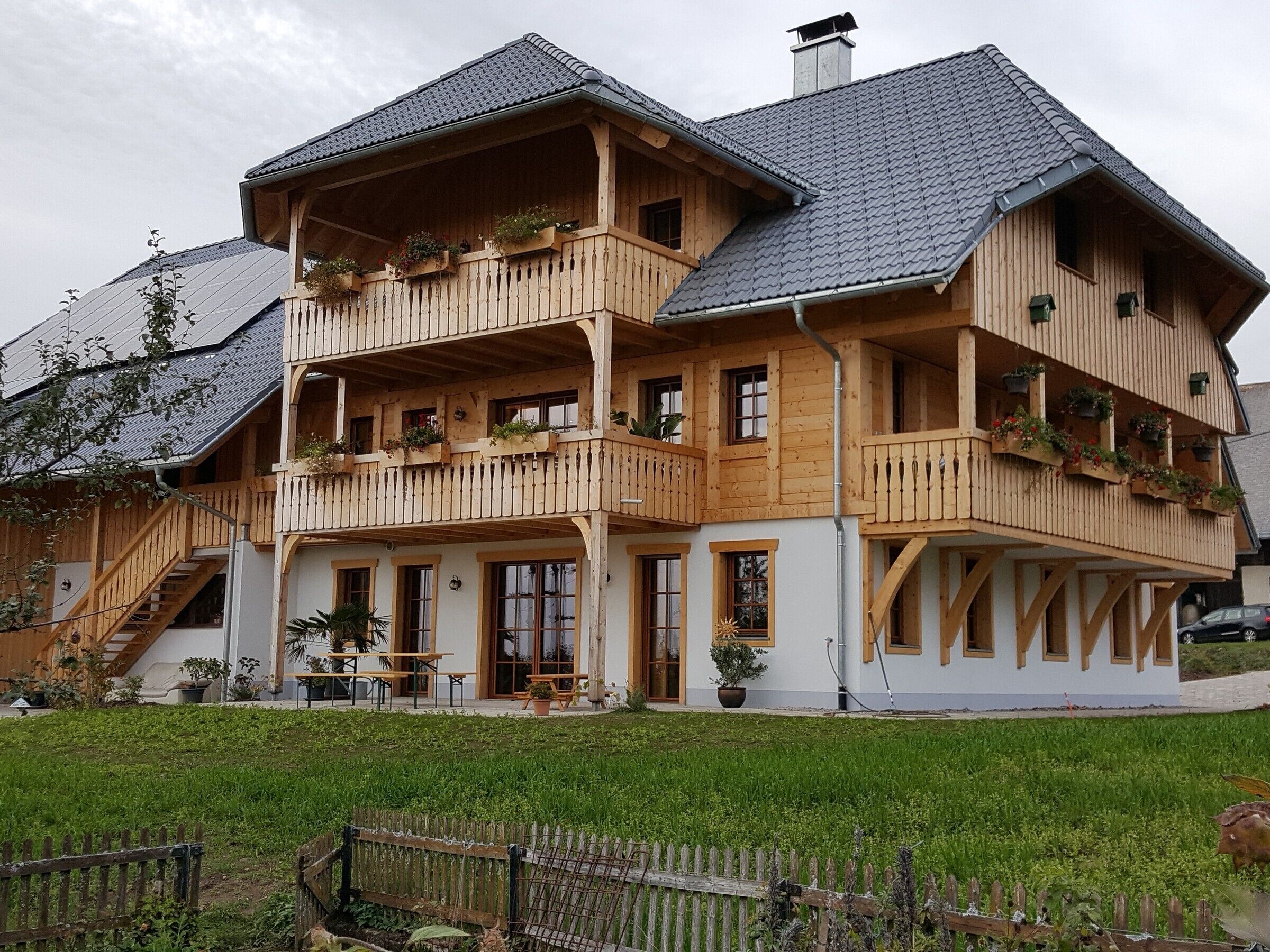 A multi-story wooden house with balconies, a staircase, and a garden.