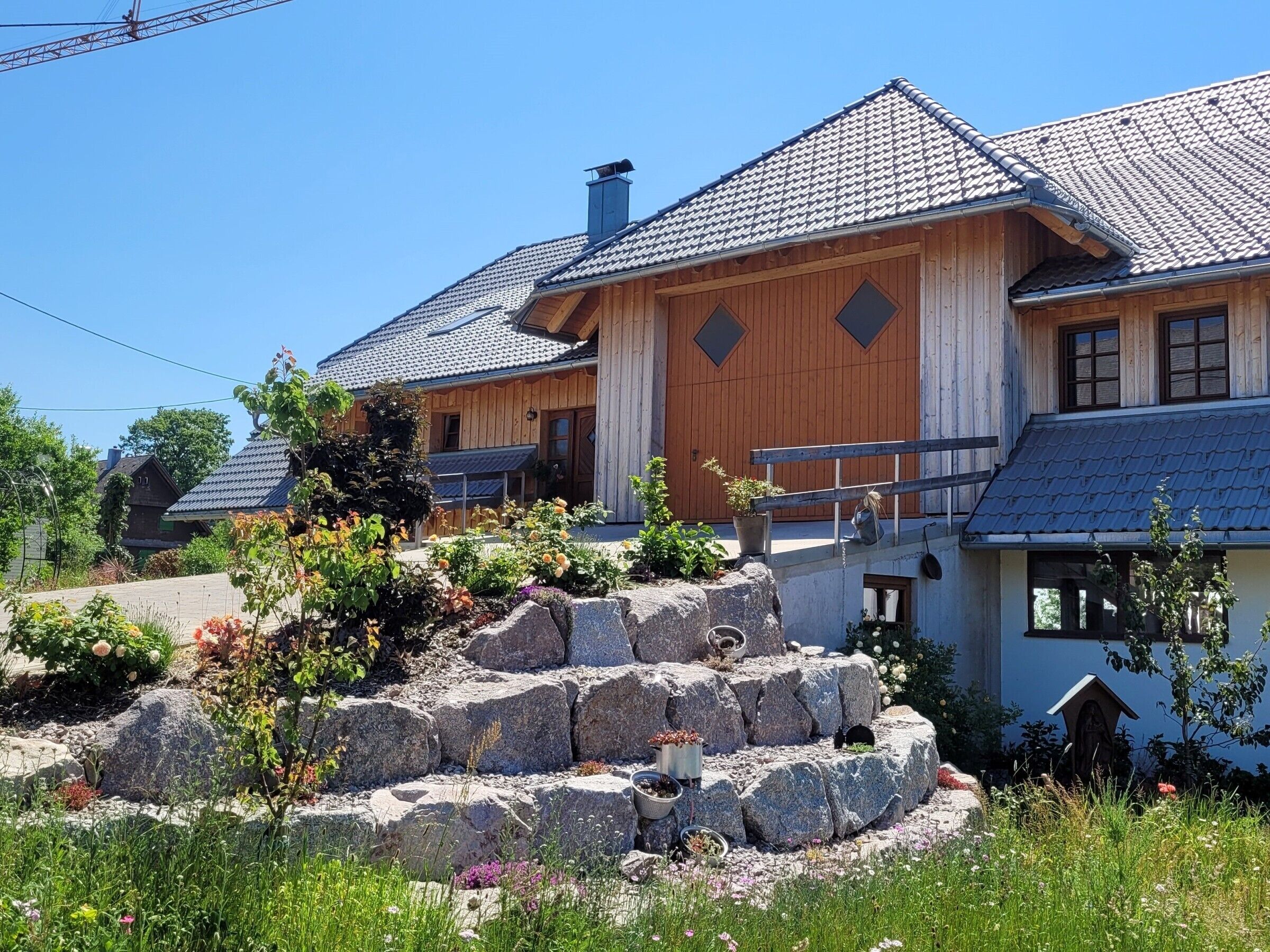 A wooden house with a tiled roof, a stone staircase, and a garden with various plants and flowers.