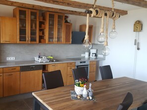 Uma cozinha com armários de madeira, uma mesa de jantar com cadeiras, uma cafeteira e um lustre.