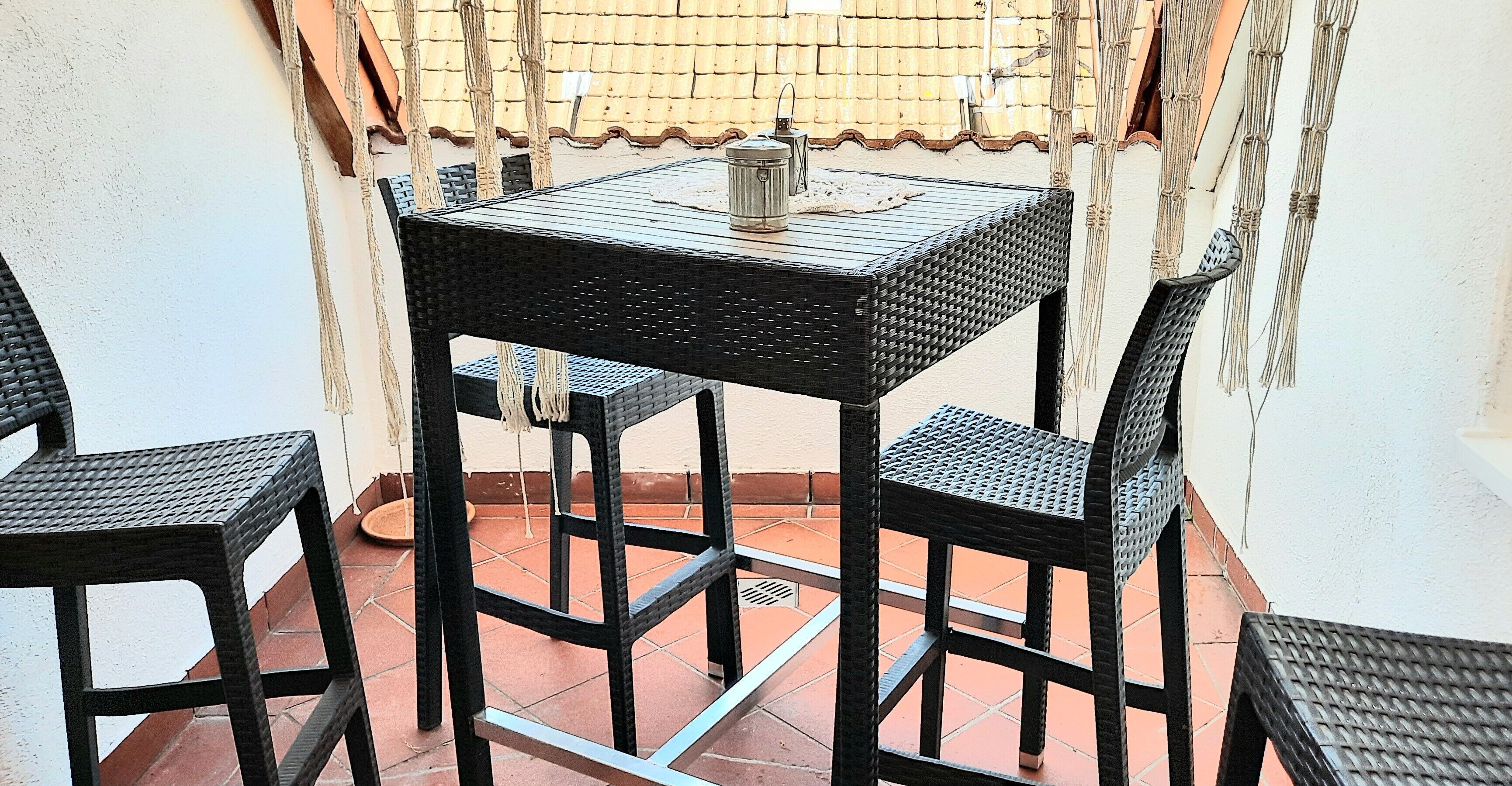 Een klein terras buiten, met een tafel en twee stoelen, een metalen lantaarn en een bamboe schutting.