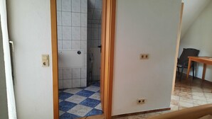 Una habitación con piso a cuadros, una puerta que da a un baño con ducha y una mesa con sillas.