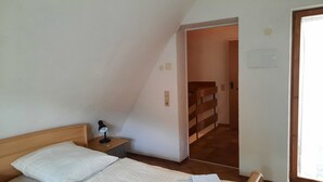 Un dormitorio con cama, mesita de noche, lámpara, puerta que da a una escalera y ventana.