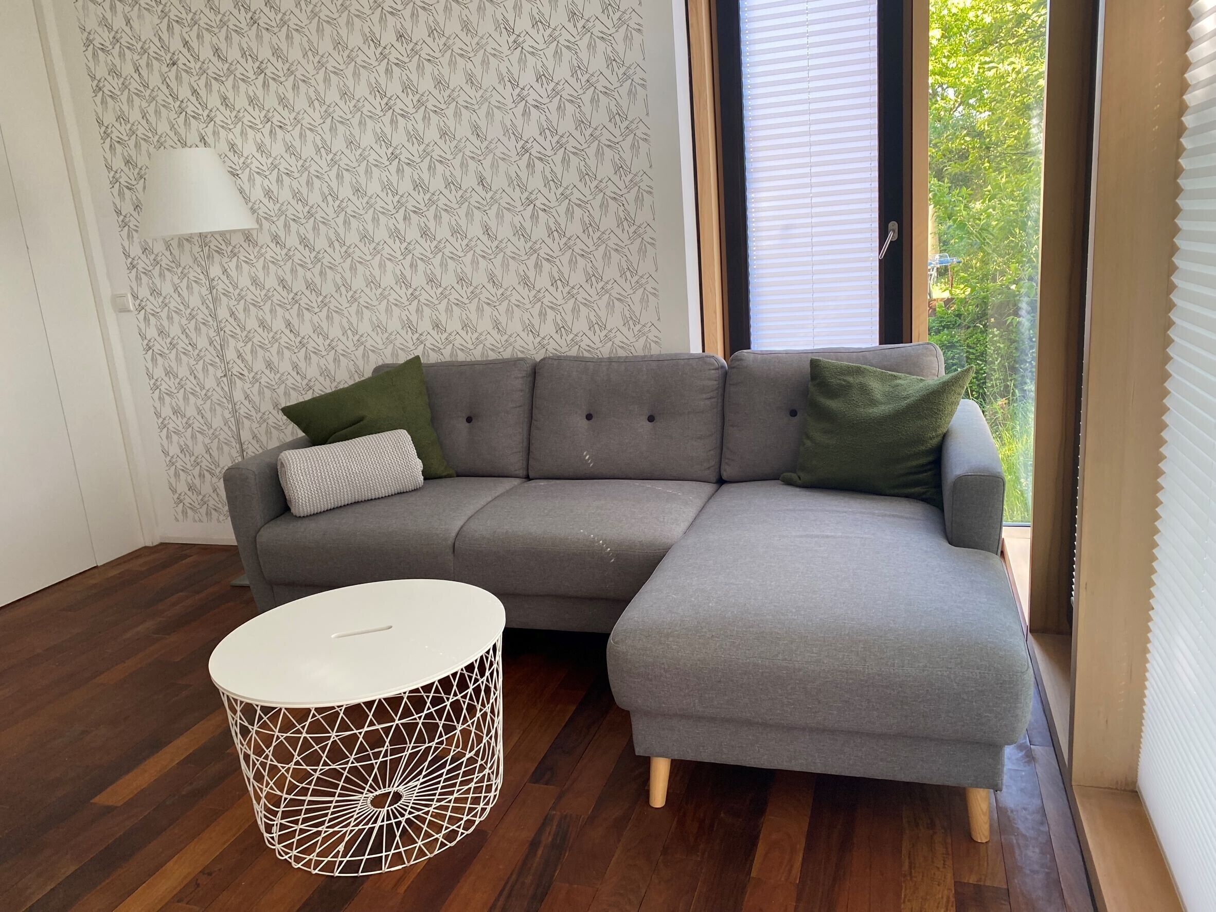 Een moderne woonkamer met een grijze modulaire bank, een rond wit bijzettafeltje en een behang met patroon.