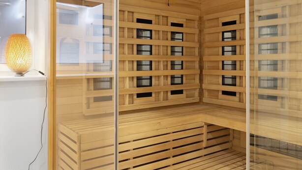 Un sauna avec des bancs en bois et une paroi en verre, une lampe en osier et un ventilateur de plafond.