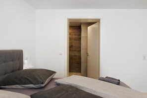 Ein modernes Schlafzimmer mit einem Bett, einem Nachttisch und einer Holztür zu einem Duschbereich.