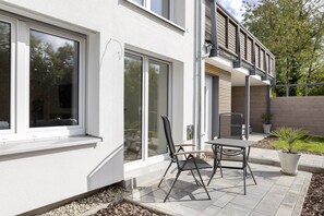 A modern house with large windows, a patio with a table and chairs, and a small garden area.