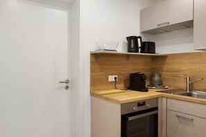 A compact kitchen with a wooden countertop, a built-in oven, a dishwasher, a coffee maker, and a kettle.