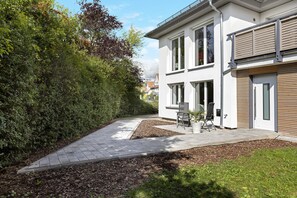 Ein modernes Haus mit befestigter Auffahrt, einer Terrasse mit Gartenmöbeln und einem gepflegten Garten.