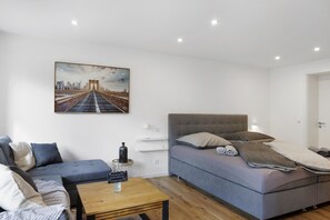 A modern bedroom with a bed, a sofa, a small table, and a painting of a bridge.