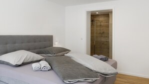 Une chambre à coucher moderne avec un lit, des oreillers, une table de chevet et un espace douche.