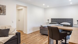A modern, well-lit room with a bed, a sofa, a dining table, and a chair.