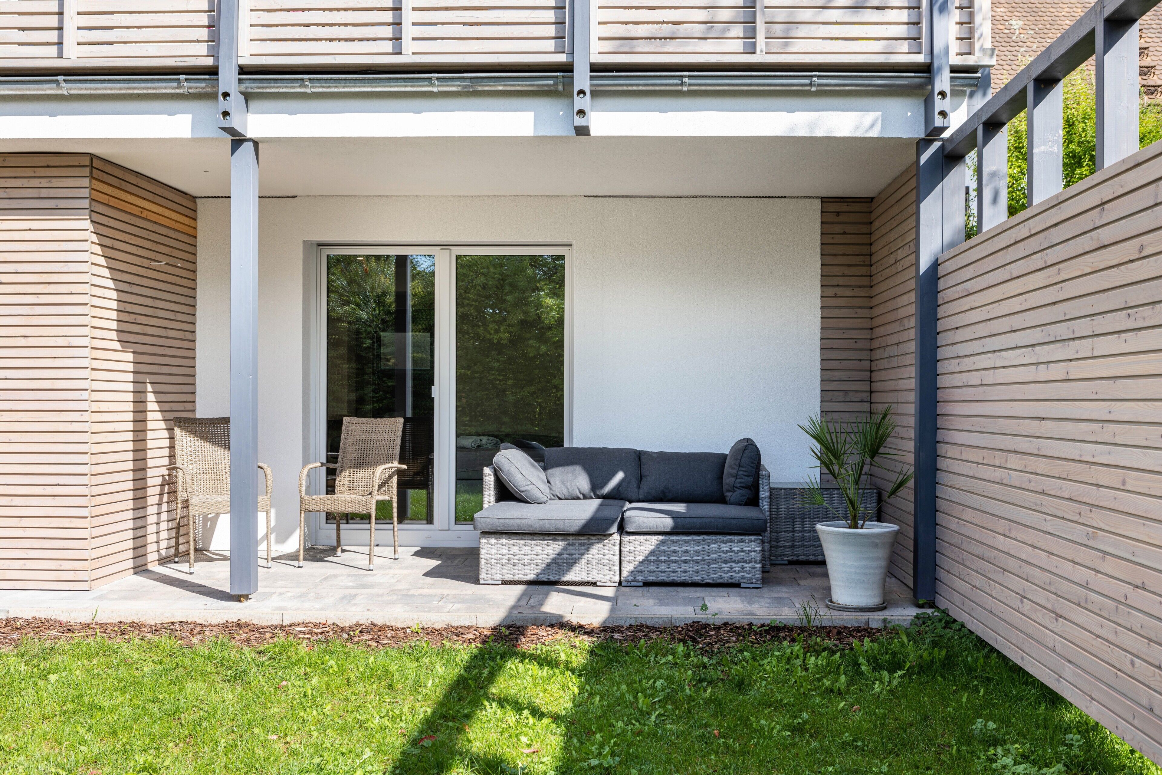 Un espace extérieur moderne aménagé avec un canapé, des fauteuils et une plante en pot.