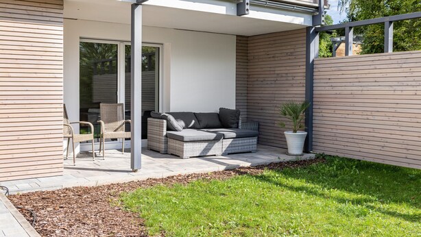 A modern outdoor patio with a wicker sofa, two chairs, and a potted plant.