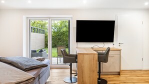 A modern room with a bed, a desk with two chairs, a television, and a sliding glass door leading to a garden.