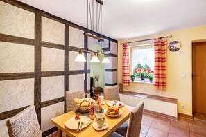 Un coin repas avec une table en bois dressée pour quatre personnes, un luminaire suspendu et une fenêtre avec des rideaux.