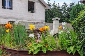 Ein Garten mit verschiedenen Pflanzen und Blumen, eine Ziegelmauer und ein Gebäude im Hintergrund.