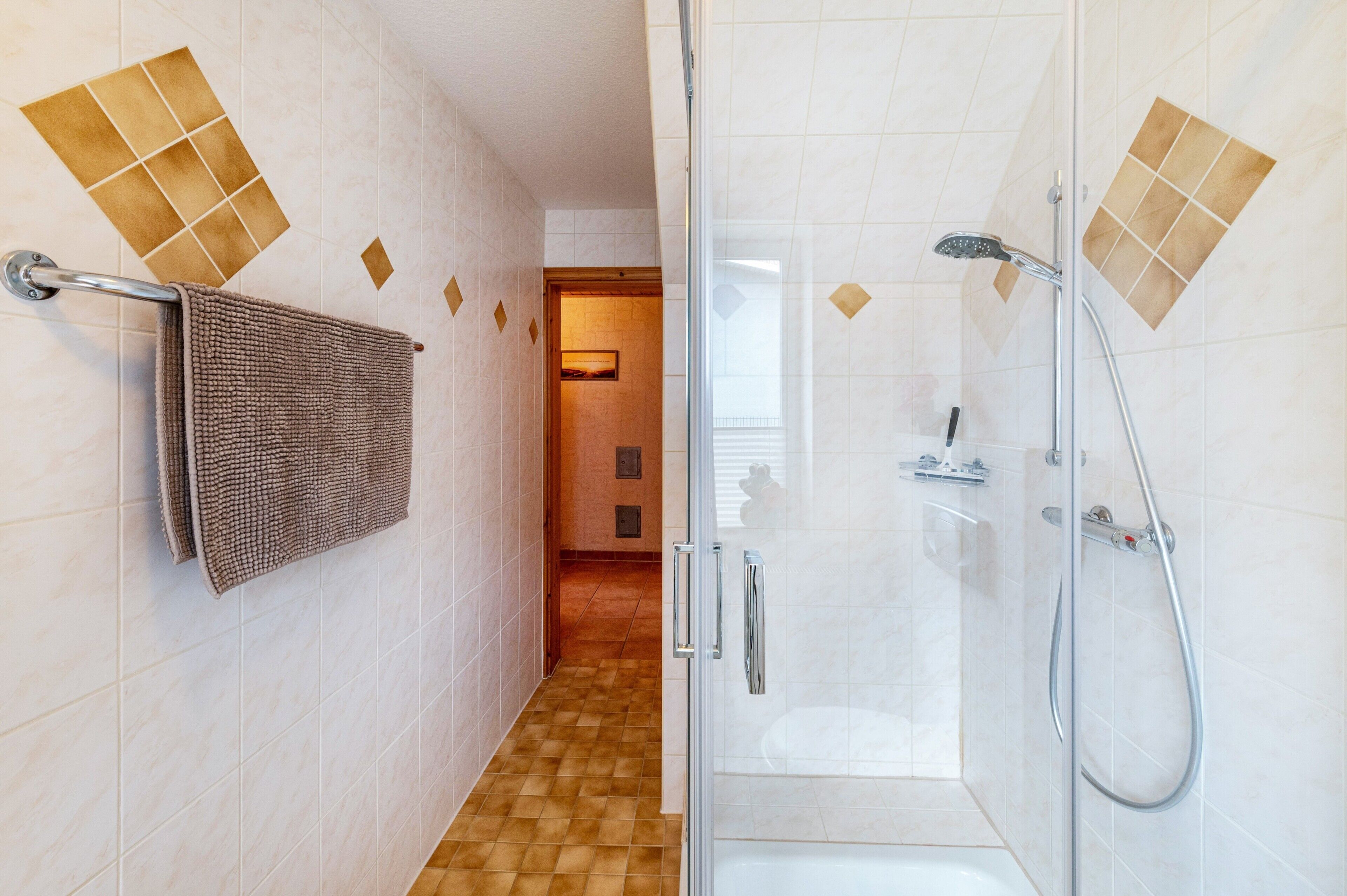 A bathroom with a glass shower enclosure, a towel rack, and a tiled floor.