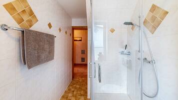 A bathroom with a glass shower enclosure, a towel rack, and a tiled floor.