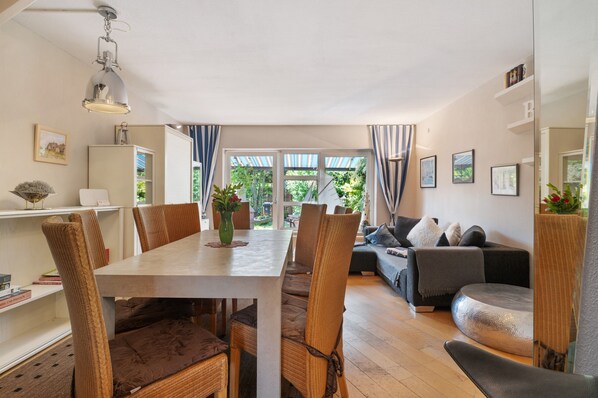 A dining area with a table and chairs, a sofa, and a view of greenery outside.