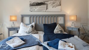 A double bed with two nightstands, each with a lamp, and a wall-mounted picture of a beach scene.