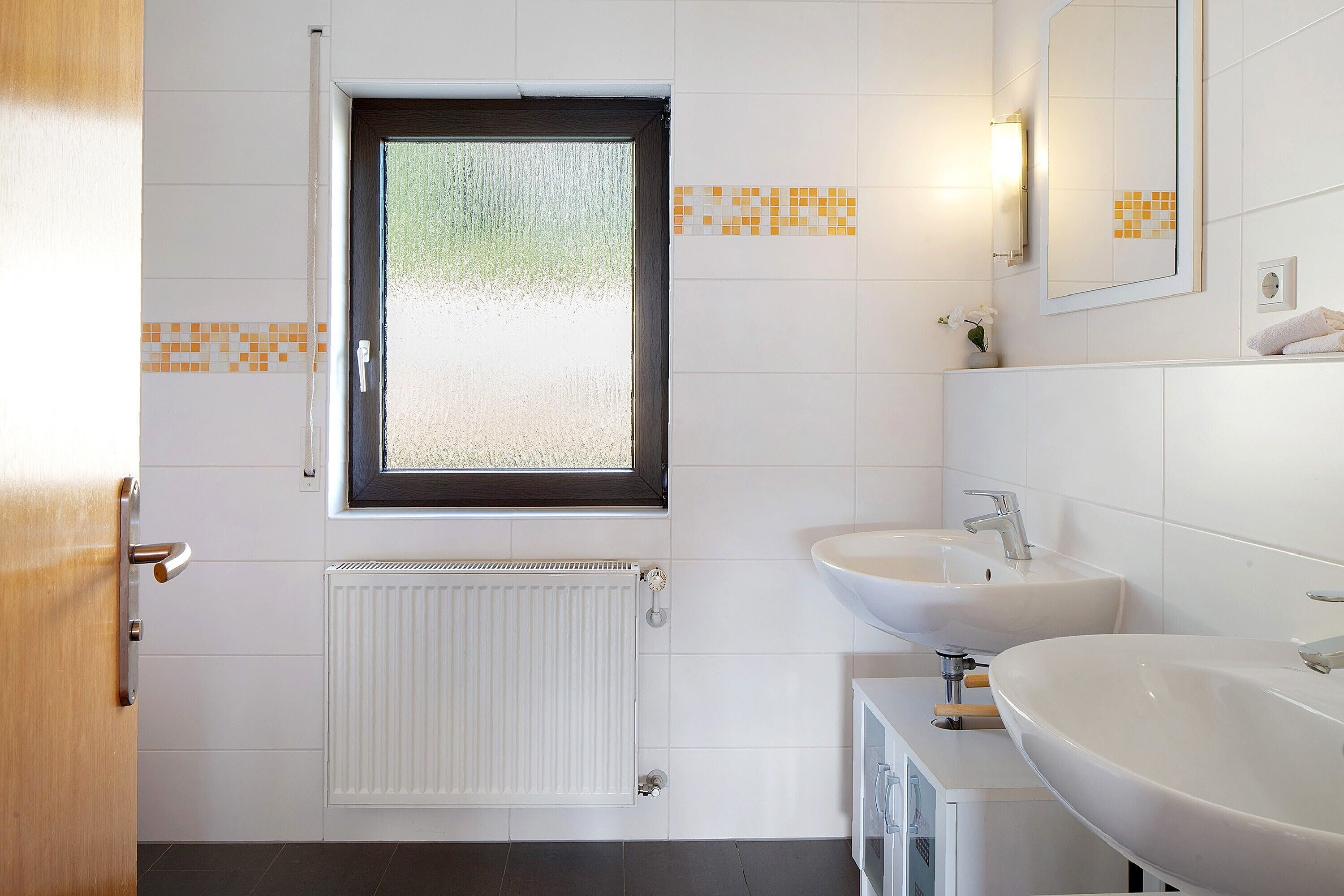 Un baño con ventana, dos lavamanos, un espejo y un radiador.
