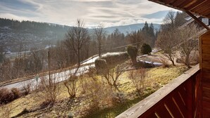 A view from a wooden balcony overlooking a valley with a river, trees, and distant mountains.