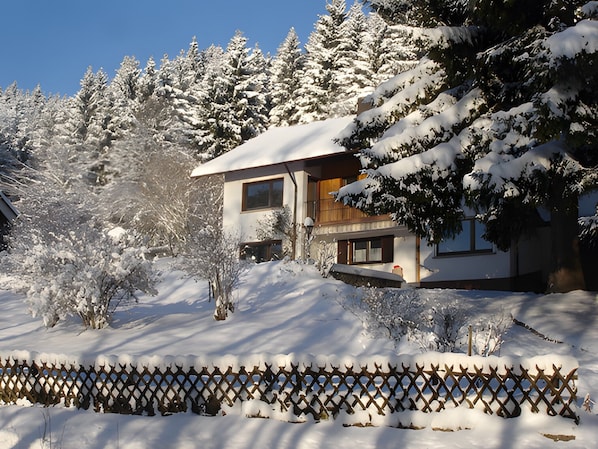 Un edificio cubierto de nieve con fachada de madera, rodeado de árboles cargados de nieve.