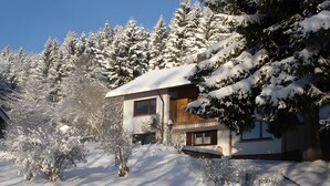 Ein mit Schnee bedecktes Gebäude mit einer Holzfassade, umgeben von schneebedeckten Bäumen.