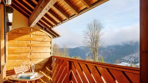 Ein Holzbalkon mit Tisch, zwei Stühlen und Blick auf eine Berglandschaft.