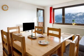 Ein Essbereich mit einem Holztisch, Stühlen, einem Fernseher und einem Fenster mit Blick auf eine verschneite Landschaft.