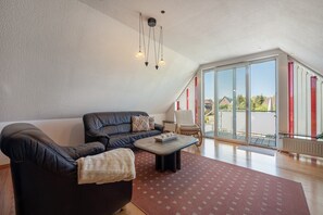 Ein modernes Wohnzimmer mit einer Ledersofa, einem Couchtisch und einer großen Schiebeglastür, die auf einen Balkon führt.