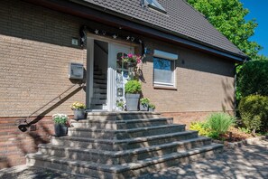 Ein Backsteinhaus mit weißer Tür, Steinstufen und Blumentöpfen.