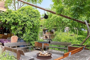 Un espace extérieur rustique aménagé avec un foyer, des bancs en bois et une balançoire suspendue.