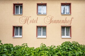 A building with the name 'Hotel Sonnenhof' and six windows with curtains.