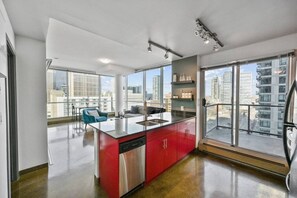 A modern kitchen with a red island, stainless steel appliances, and large windows offering city views.
