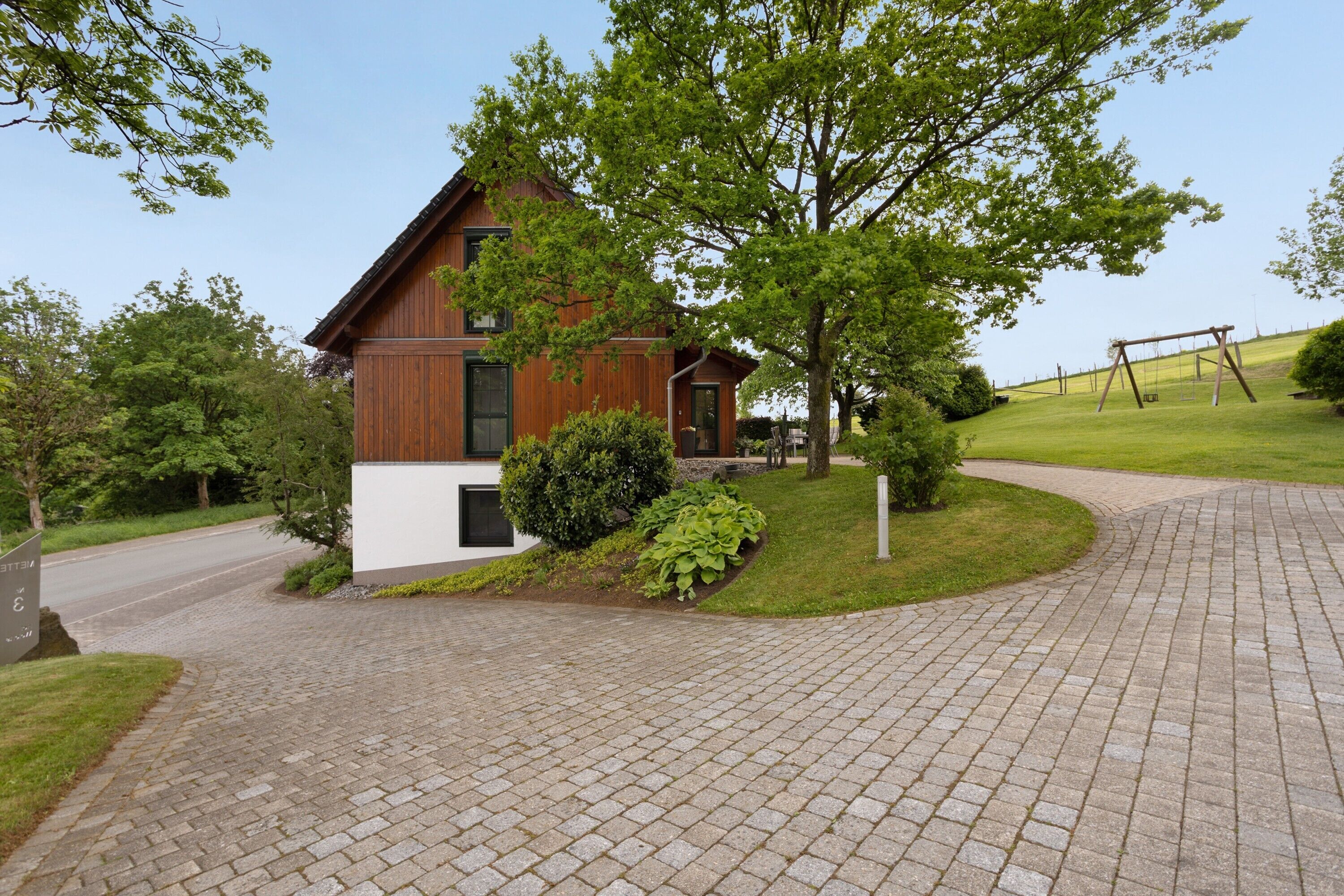 Une maison moderne avec une allée pavée en briques, une balançoire et une pelouse bien entretenue.