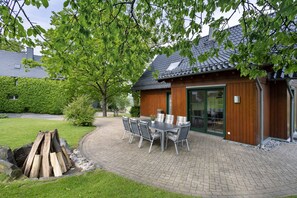 A patio with a table and chairs, a fire pit, and a building with a tiled roof and wooden siding.
