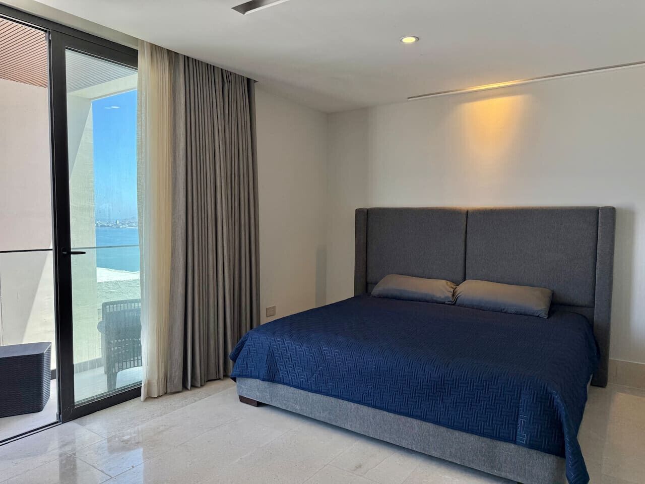 Une chambre à coucher moderne avec un grand lit, une porte-fenêtre coulissante donnant sur un balcon et une vue sur la mer.