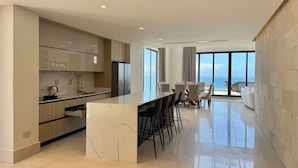 Una cucina moderna con isola in marmo, sgabelli da bar e zona pranzo con vista sull'oceano.