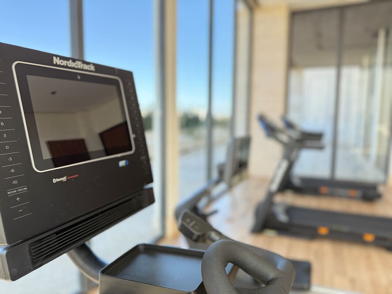 Een NordicTrack trainingsapparaat met een digitaal scherm, in een sportschool met grote ramen en loopbanden op de achtergrond.