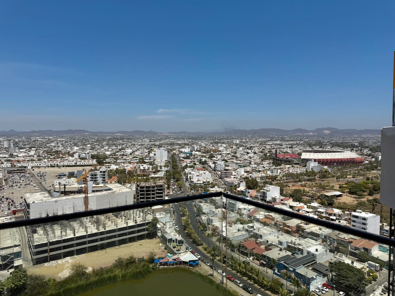 A cityscape with a view of a large building under construction, a river, and a stadium in the distance.