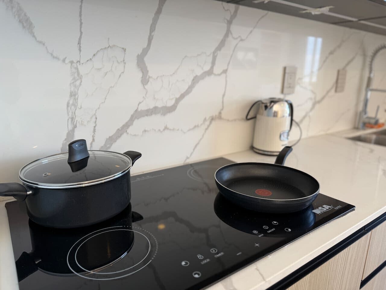 A kitchen with a black induction cooktop, a pot with a lid, and a frying pan.