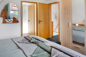 Een slaapkamer met een bed, een houten garderobe, een spiegel en een deur naar een andere kamer.