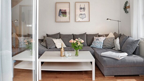 Una sala moderna con un sofá gris, una mesita de centro blanca y cuadros en la pared.