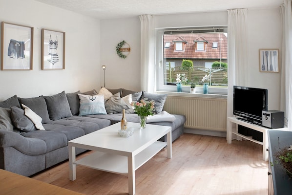 A living room with a grey sofa, white coffee table, and a TV on a white stand.